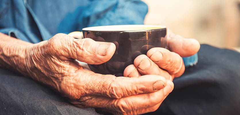 Bilden föreställer en äldre mans händer och han håller i kaffekopp.