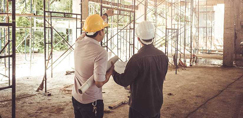 Byggarbetare står med bygghjälmar på huvudena och håller i byggritningar.