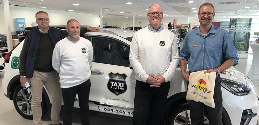 Taxi Allians delägare och C4 Energis energisäljare Martin Holmén poserar framför vit eltaxibil.