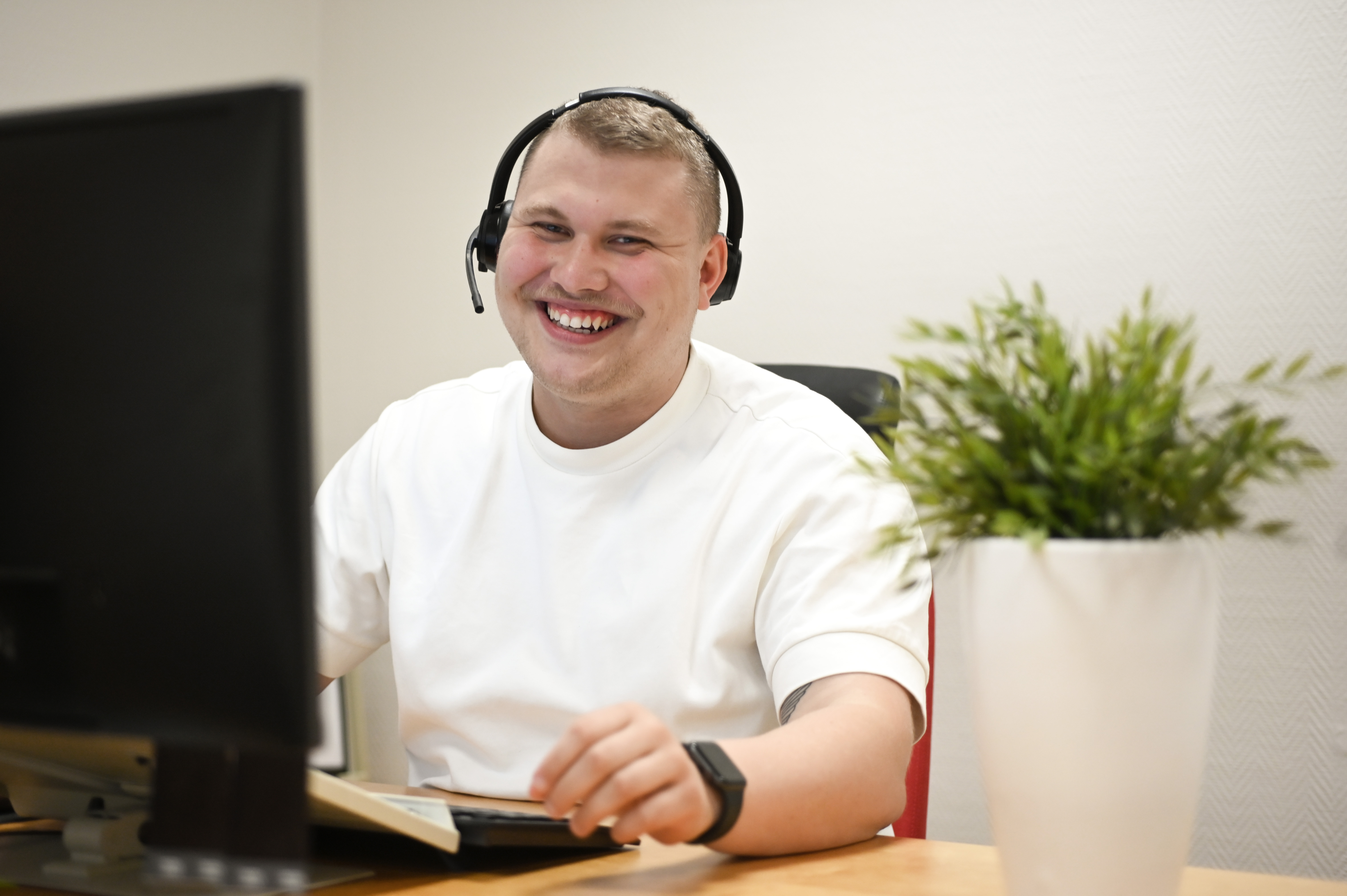 En leende man i kundservice sitter med headset framför en dator